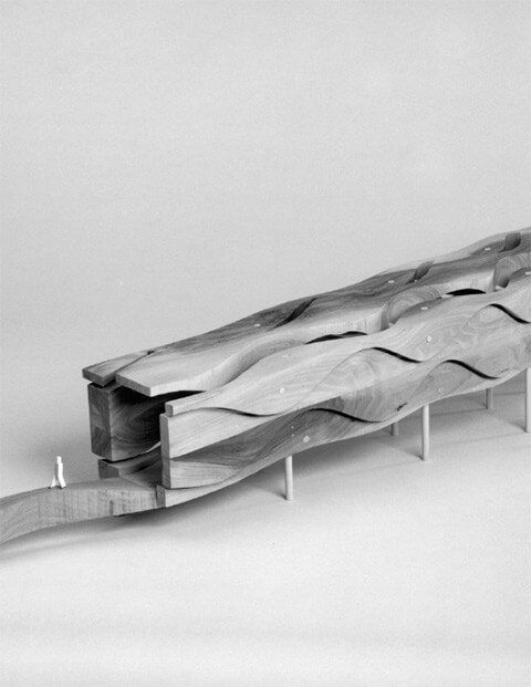 Die Sinusgasse, 1993, Nussbaumholz, Länge 155 cm, Breite 20 cm, Höhe 30 cm. Modell Mst. 1:50 für begehbare Ausführung, Foto Walter Grunder. Beschreibung: Die Sinusgasse ist der Architektur genaues Gegenteil. In ihr gibt es weder Horizontale noch Vertikale und weder Gerade noch Strecke. Masse werden eher physikalisch als stereometrisch empfunden. Längen werden Wellenabschnitte, Breiten werden Amplituden. Der Ort der Ruhe, Kennzeichen jeder Architektur, fehlt nicht nur, es gibt auch den Ort als solchen nur als rechnerischen Funktionswert, ohne festes Bezugsmoment. Wer sich in der Sinusgasse aufhält, einem Konstrukt aus progressiv pulsierenden Sinuskurven, halluziniert das Gefühl, ein Subjekt des fliessenden Raumes zu sein.